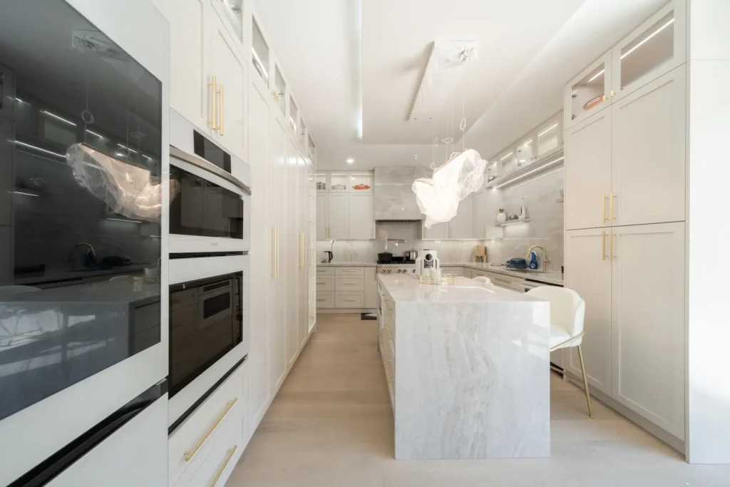 Long custom kitchen with integrated wall ovens, tall cabinetry and a marble waterfall island